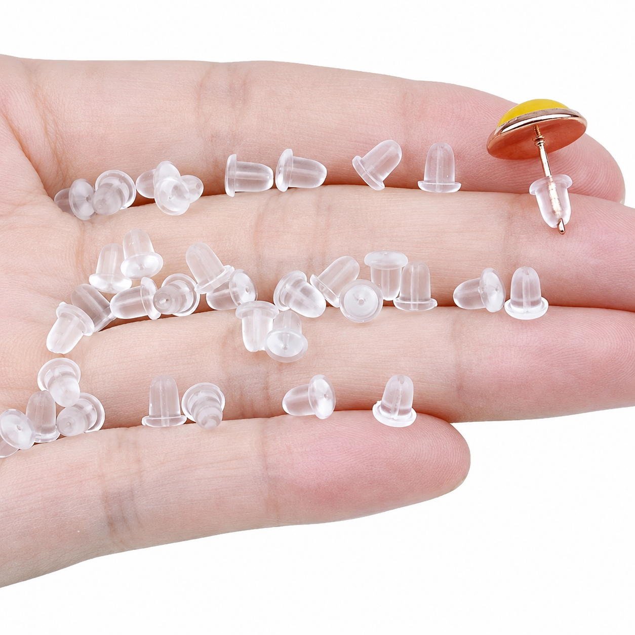 A hand holding multiple small clear silicone earring backs, with one earring back shown upright on the fingertip to demonstrate its shape and post.