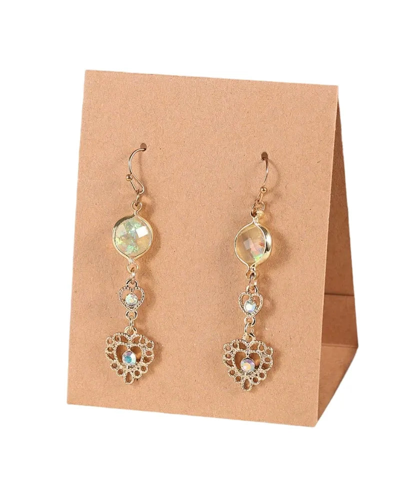 A pair of gold-toned dangle earrings with iridescent round and marquise-cut stones and an ornate filigree heart pendant, displayed on a tan paper stand against a white background.