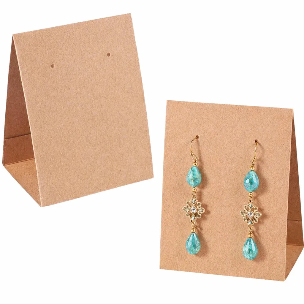 A pair of gold drop earrings with light blue teardrop gemstones and clear crystal details, displayed on a brown kraft paper stand against a white background.