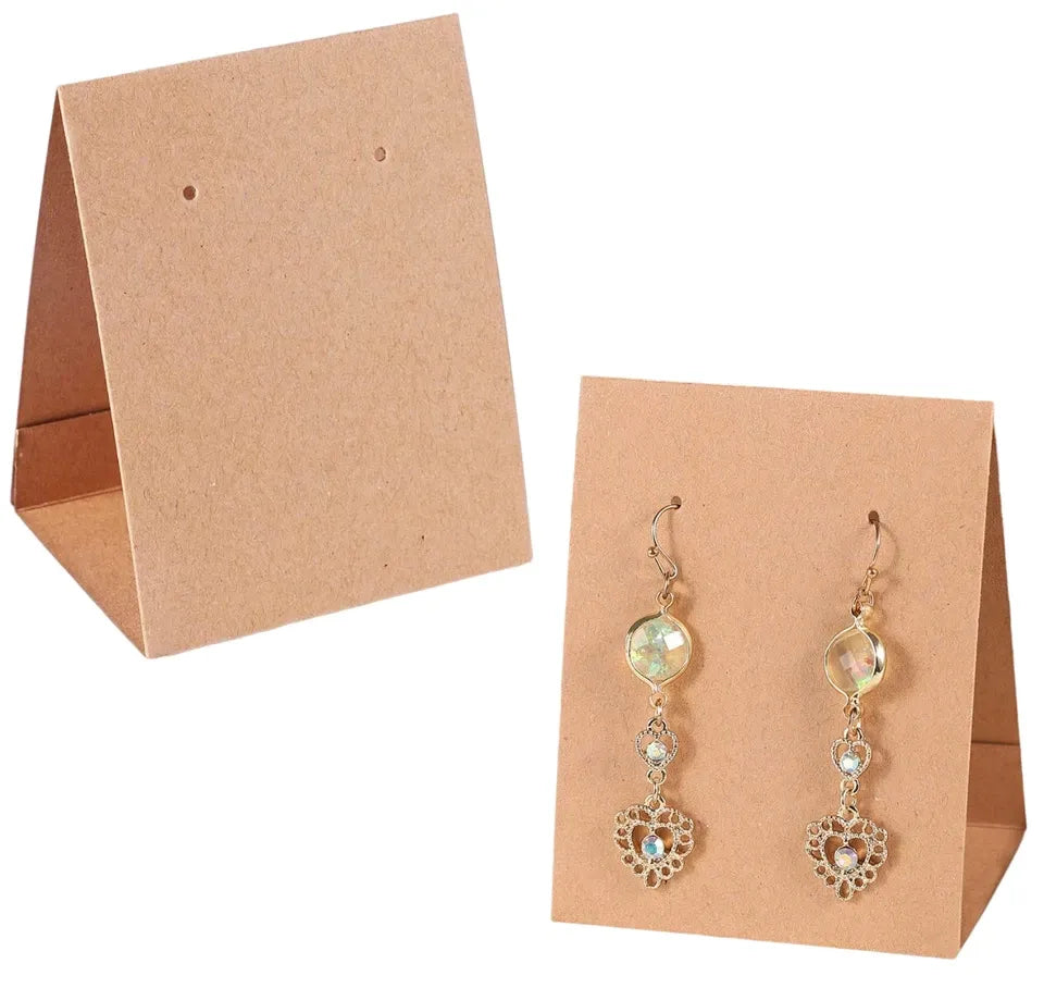 A pair of dangling earrings displayed on tan cardboard card holders against a white background. The earrings have gold-toned metal hooks and settings with iridescent round beads and heart-shaped dangling charms with small clear stones.