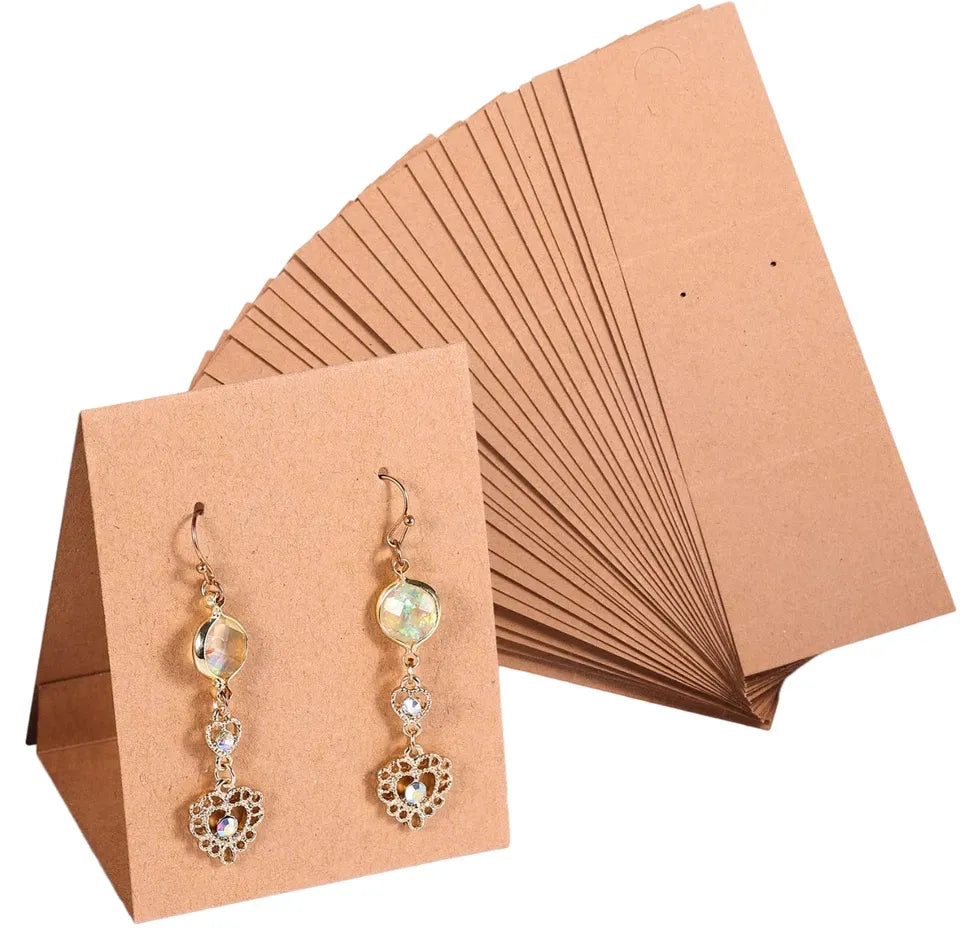 A pair of dangling earrings displayed on a tan kraft paper card, with a matching stack of tan display cards behind them on a white background.