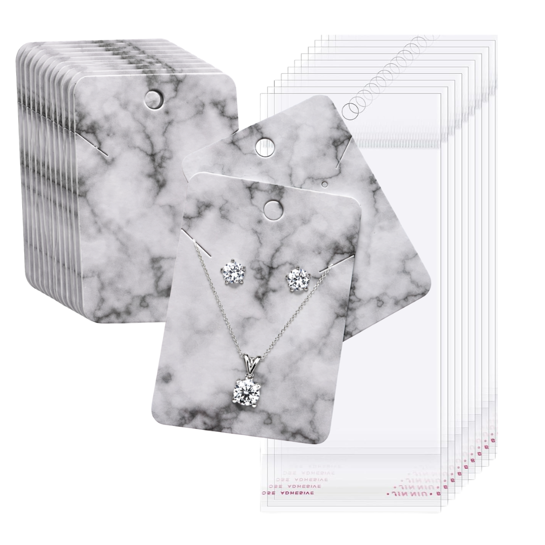 A set of jewelry display cards with a white and gray marble pattern, shown alongside clear plastic pouches. The front card features a silver necklace and matching stud earrings with clear gemstones.