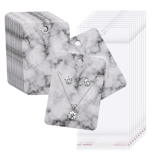 A set of jewelry display cards with a white and gray marble pattern, shown alongside clear plastic pouches. The front card features a silver necklace and matching stud earrings with clear gemstones.