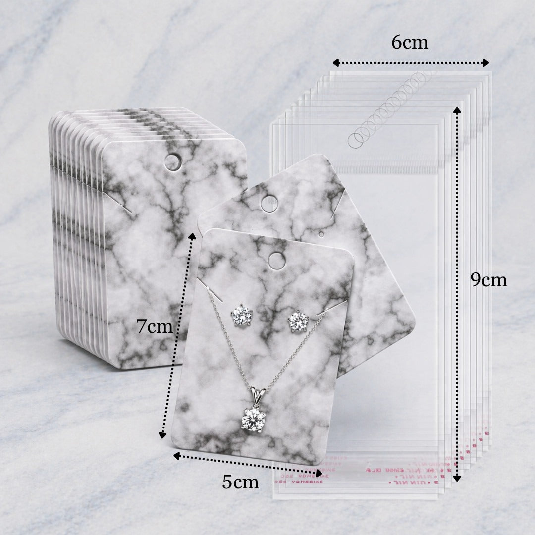 Jewelry display cards shown with dimension labels: a stack of marble-patterned cards, one front card holding a necklace and matching earrings, and a sheet of clear sample cards with measurements marked 6cm, 7cm, 9cm, and 5cm on a light marble surface.