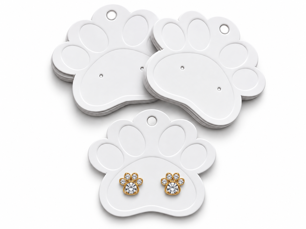 White paw-shaped jewelry display cards with two small stud earrings displayed on one card. The earrings have gold-tone paw-shaped settings with clear round gemstones.